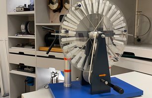 Eine Influenzmaschine steht auf einem kleinen Tisch vor dem elektrischen Kabinett. Im Hintergrund sind weitere Versuche und Geräte zur Demonstration von elektrischen Versuchen zu sehen. 