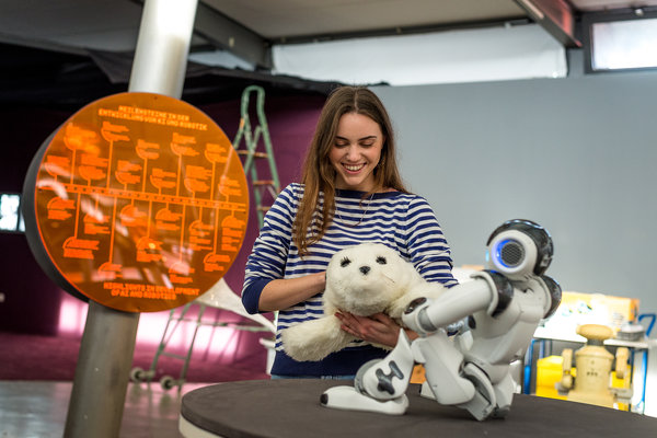 Junge Frau mit Stoff-Seehund und Roboter.